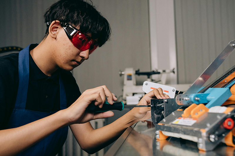 A young person wearing safety goggles and working on some equipment with a a screwdriver