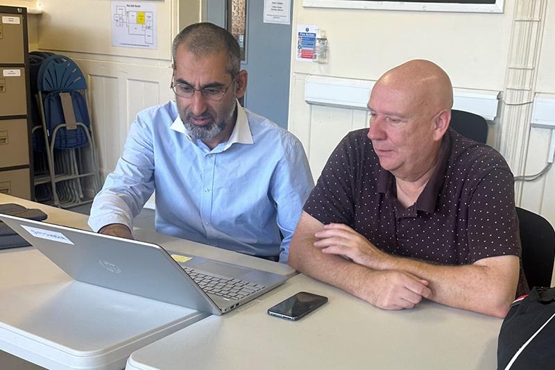 Two people sat at a desk using a laptop