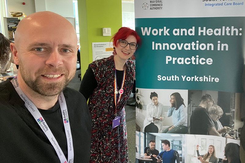 Two people stood in front of a banner that reads 'Work and Health: Innovation in practice"