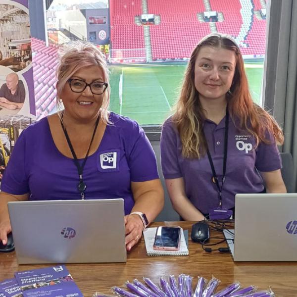 Two ladies sat together smiling with their laptops in front of them