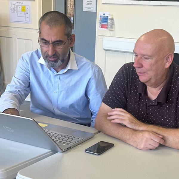 Two people sat at a desk using a laptop