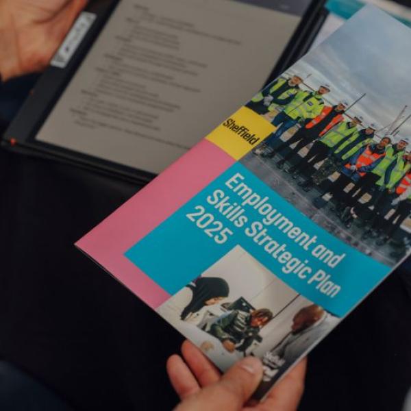 A hand is holding a booklet with a photo of group of people stood in a line wearing hi-visibility jackets on the cover. The title reads: Employment and Skills Strategic Plan 2025